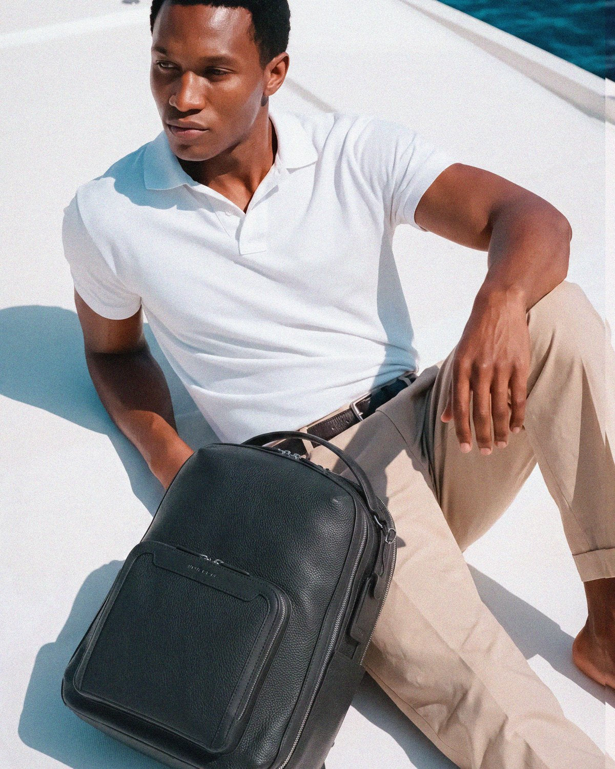 Man seated on a yacht deck beside the Pilot backpack in Jet Black