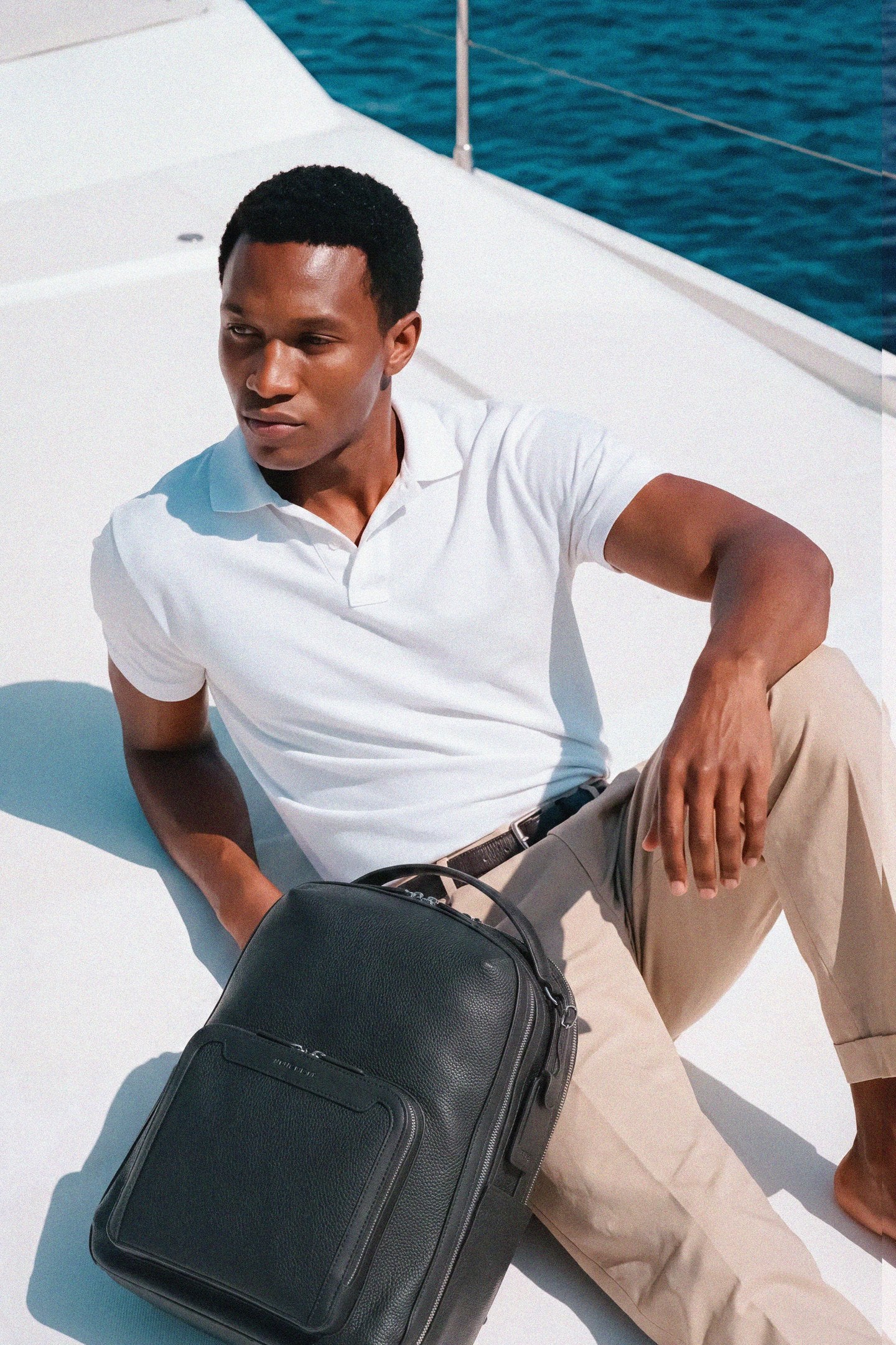 Man seated on a yacht deck beside the Pilot backpack in Jet Black
