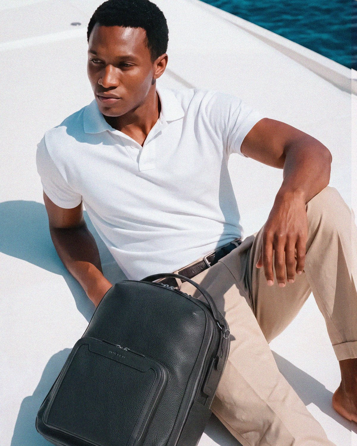 Man seated on a yacht deck beside the Pilot backpack in Jet Black