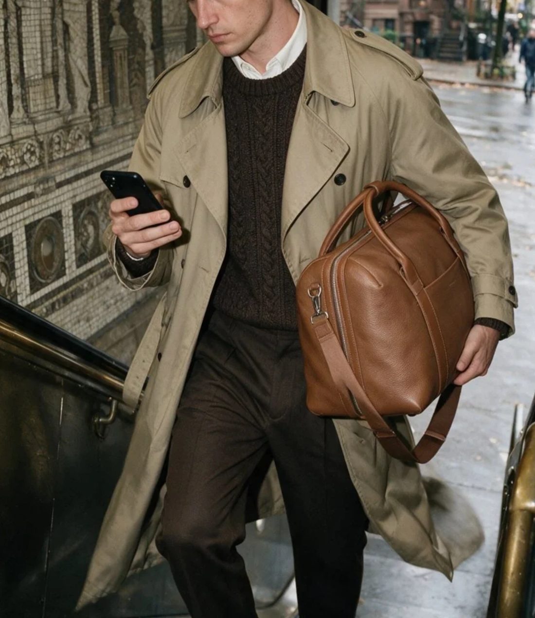 Man in a trench coat carrying a leather duffle under his arm